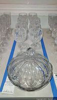 Photo showing 8 Waterford Crystal wine glasses arranged behind a clear cut glass bowl with lid on a table.