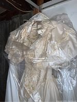 Full view of ivory wedding gown showing lace, satin, and bead detail wrapped in plastic