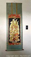 Full view of the antique Chinese scroll wall hanging suspended against a white wall showing the entire artwork and fabric mount with hanging cord above.