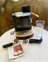 Full view of DeLonghi espresso maker with water reservoir, drip tray, accessories, and manual on table.