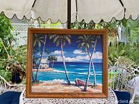 Front view of framed tropical print showing palm trees, beach hut, boat, ocean and sky.