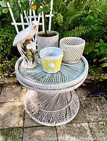 Outdoor garden collection setup including white wicker table with glass top, two white trellis panels, ceramic bird figurine, fake lemon tree, yellow and lattice ceramic pots.