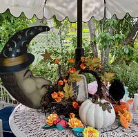 Large hanging witch moon face decoration with a star, black with gold accents, on an outdoor table with other Halloween decorations