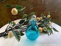 Blue glass pinch decanter with stopper placed on table with faux lemon branches in background