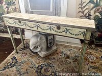 Front angle view of hand painted neoclassical console table with garland motifs and elephant base on patterned rug