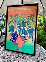 Full photo of framed Peter Max "Life is So Beautiful" poster displayed outdoors on a metal table with greenery background