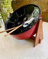 Full view of black minipan steel drum with red sides on a wooden stand with two mallets resting inside.