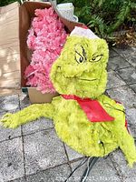 Pink flocked Christmas tree parts and blow-up Grinch laid out with some dirt visible on the Grinch