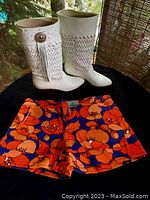 Pair of white leather fringe cowboy boots with perforated pattern, alongside floral orange and blue Judith March short shorts.