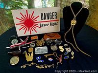 Top-down view of the lot showing the bolo tie on a black velvet display, multiple pins, badges, spectacles, and the 'DANGER laser light' sign in the background.