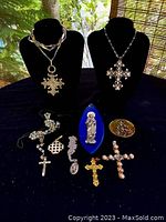 Full lot overview showing all 9 vintage religious pieces arranged on black cloth including cross pendants, religious plaques and pins.