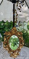 Ornate vintage Florentine mirror with gold painted floral and leaf carvings surrounding oval glass mirror hanging outdoors.