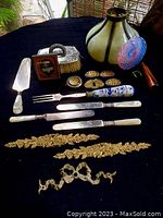 Overview photo showing the majority of the items on black fabric including grooming brush, daguerreotype frame, decorative buttons/appliques, cutlery with decorative handles, and gold-tone appliques.