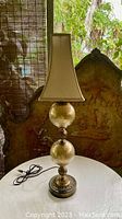Vintage two-globe golden Murano glass table lamp with brass base and fittings, beige fabric lamp shade placed on bulb, photographed on white table with decorative screen backdrop.