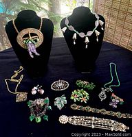 Full view of the 13 vintage jewelry pieces arranged on a black cloth including necklaces on bust displays, brooches, bracelets, and earrings.