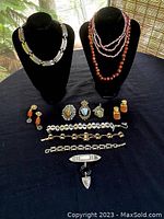 Full view of 12 vintage jewelry pieces on a black cloth with 2 display busts including necklaces, brooches, bracelets, and earrings.