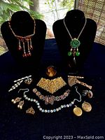 Full layout of vintage jewelry collection on display with two black busts holding necklaces. Various brooches, earrings, lockets, and pins arranged in front.