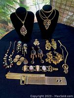 Full lot showing 13 pieces of vintage jewelry on black cloth, including necklaces on busts, earrings, bracelets, and belt.