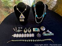 Collection of 12 vintage jewelry pieces including necklaces, bracelets, earrings, and brooches, displayed on a black surface with two necklace busts