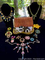 Photo showing entire lot including 13 pieces of vintage jewelry and chalet trinket box with thatched roof on black display against window background