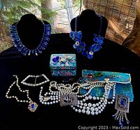 Overview of lot on black tablecloth showing two black display busts with statement necklaces, several pearl necklaces, brooch or pendant pieces, satin jewelry envelope, and lacquer trinket box.
