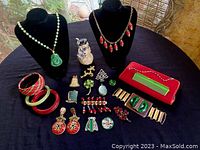 Full overview of the vintage jewelry pieces displayed on a black table with two necklace busts, including bracelets, brooches, earrings, a red purse, and a snowman figurine in background.