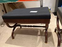 Side view of a wooden bench with black cushioned seat showing elegant curved legs and brass capped feet.