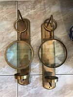 Pair of brass wall sconces shown from front with magnifying glasses attached.