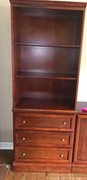 Front view of tall wooden bookshelf unit with three shelves and three drawers with round metal knobs.
