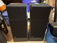 Front view of both speakers side by side on concrete floor with storage bins in background