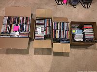 Four open boxes filled with music CDs arranged neatly on carpet floor, showing the overall quantity and condition of the collection.