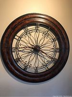 Full view of the round metal wall clock showing Roman numerals and decorative wire center.