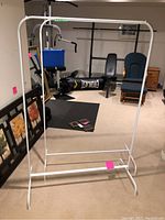 Metal clothes rack in a basement setting, showing the rectangular frame, horizontal hanging bar, and base with rounded feet.