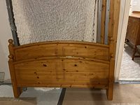 Light wood double bed frame leaning against a wall with visible wood grain and turned post details.