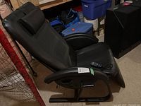 Angled left side view of the black massage recliner showing seat, armrest and attached remote on the cushion