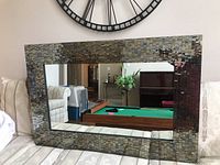 Full front view of the rectangular mirror showing the mosaic glass tile frame and the reflective mirror glass center, placed on a sofa with a wall clock above.