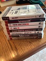 Photo showing stack of eight PS3 game cases with titles visible on spine.