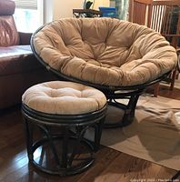 Rattan papasan chair and matching stool with cushions seen from front angle in a living room setting on hardwood floor.