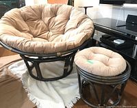 Full view of rattan papasan chair and matching stool with tan cushions on light colored rug indoors.