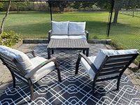 Front view of the outdoor seating area with two chairs, bench and table on patterned outdoor rug