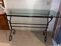 Clear glass top with beveled edges on ornate dark metal frame with curled legs and brass accent spheres.