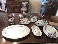Overview of 10 pieces on table showing various silver plated and copper plate serving items including coffee pot, trays, dishes, and shakers.