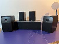Six home theatre speakers arranged on a purple table surface showing overall set.