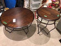 Two round tables with dark wood tops and black metal frames, coffee table larger than side table, both showing surface wear and scratches