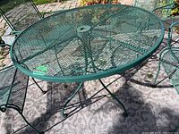 Full view of weathered vintage round outdoor metal table made of green metal mesh with umbrella hole.