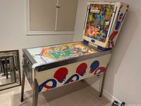 Side view of pinball machine showing white cabinet with red and blue helmet graphics and chrome legs
