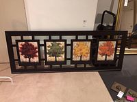 Wall art with four panels featuring trees with leaves in red, green, yellow, and orange, set within a dark brown wooden frame with geometric openwork.