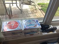 Photo showing nineteen Wii games stacked in two piles with one Wii microphone accessory in packaging.