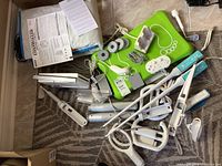 Full lot showing Nintendo Wii console, multiple controllers, wired dance pad, sensor bar, manuals laid out on a carpeted floor.