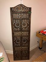 Full view of wood screen leaning against wall showing entire carved motif and shape